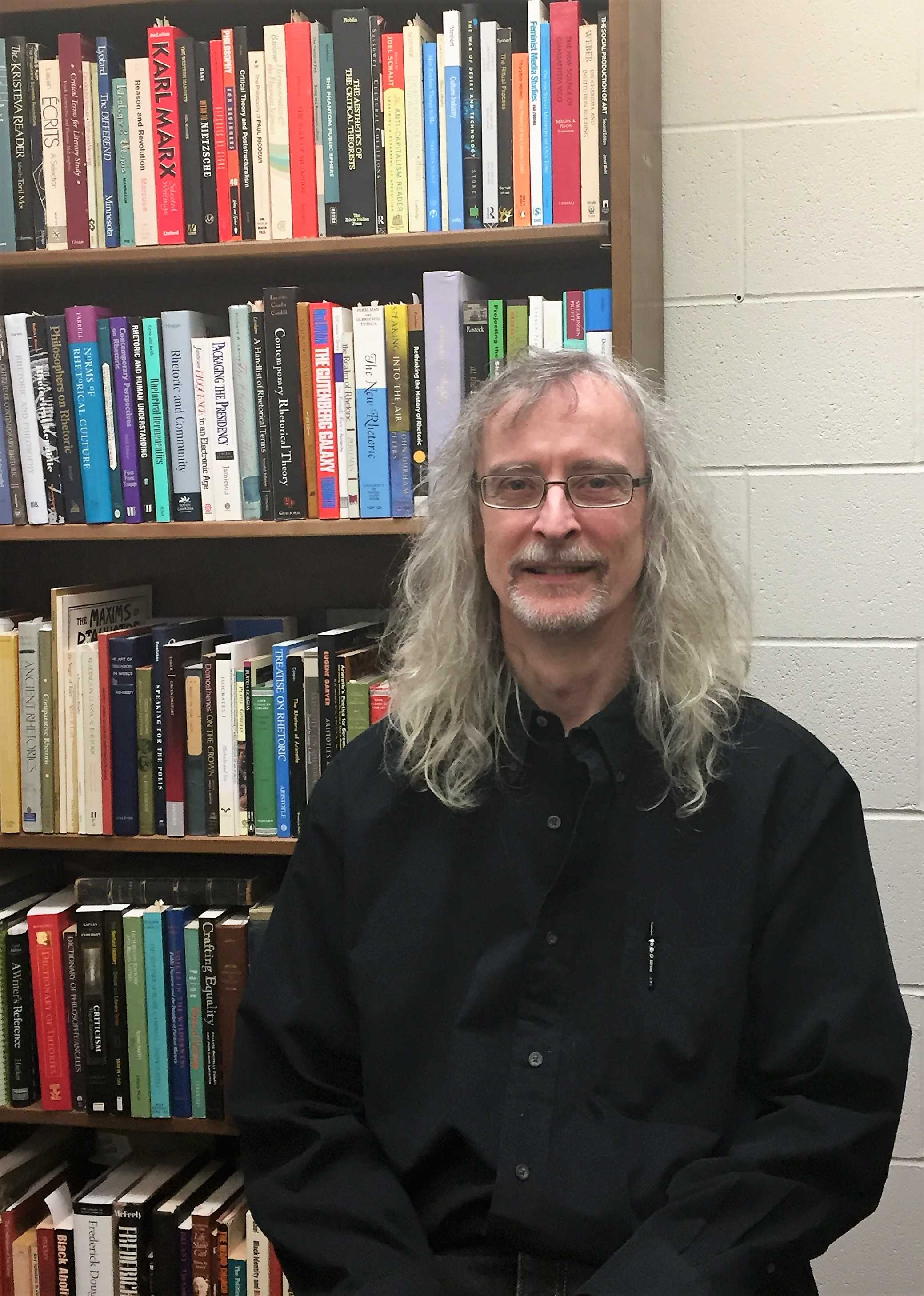 Associate Professor of Communication Arts Larry Lamber poses in front of one of his favorite things—books. PHOTO/Ashley Foor